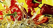 Peppers falling into water against yellow background