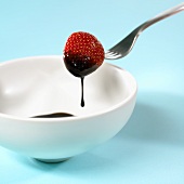 A strawberry being dipped in chocolate