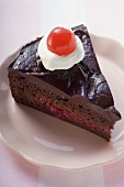 A piece of chocolate cake with cream and glacé cherry