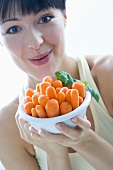 Young woman holding a bowl of baby carrots