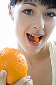 Woman with orange dragee in her mouth & orange in her hand