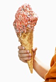 Child's hand holding large cone of strawberry ice cream