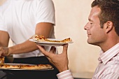 Mann hält genüsslich einen Teller mit einem Stück Pizza