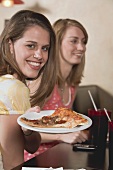 Two young women, one holding a plate of pizza