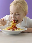 A blonde girl eating spaghetti with tomato sauce