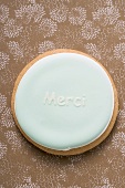 Ein pastellfarbener Keks mit Aufschrift 'Merci'