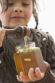 Girl taking organic honey out of jar with honey dipper