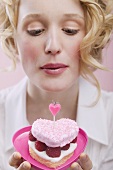 Young woman blowing out candle on raspberry cake