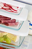 Cheese, salami & radishes in food storage boxes in fridge