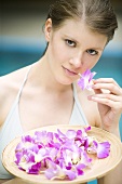 Junge Frau hält Tablett mit Blüten am Swimming Pool
