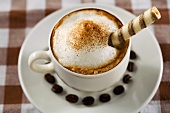Eine Tasse Cappuccino mit Waffelröllchen und Kaffeebohnen