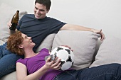 Young couple on sofa with football and bottle of beer