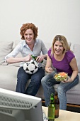 Two friends watching TV with football, beer and salad