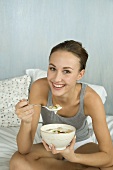 Junge Frau isst Müsli mit Joghurt im Bett