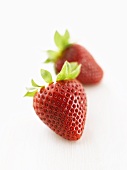 Two strawberries on white wooden surface
