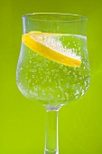 Glass of water with slice of lemon against green background