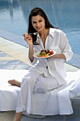 Weiß gekleidete Frau isst Salat am Swimmingpool