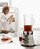 Tomato juice in liquidiser, young woman in background