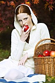 Young woman eating apple in park in autumn