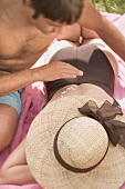 Mann cremt Frau den Rücken mit Sonnencreme ein