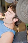 Man eating muesli bar on weight bench
