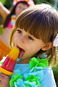 Kleines Mädchen schleckt ein Fruchteis auf Kinderparty