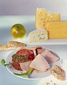 Sliced meat platter with various cheeses in the background