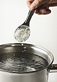Einen Löffel Salz in einen Topf mit Wasser streuen