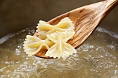 Cooked farfalle on wooden spoon above a pot