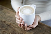 A pair of hands holding a cappuccio cup