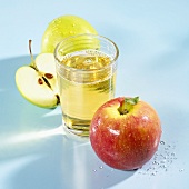 A glass of apple schorle with apples beside it