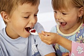 Girl putting a spoonful of yoghurt into a boy's mouth