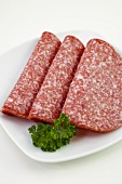 Three slices of salami with parsley on plate