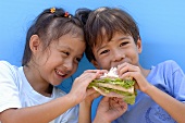 Two children eating a ham sandwich
