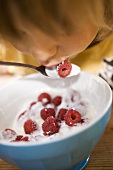 Small child eating yoghurt with fresh raspberries