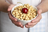 Hands holding a bowl of toasted rice breakfast cereal with cherry
