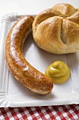 A sausage with mustard and bread roll on paper plate