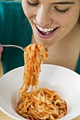 Woman eating ribbon pasta with tomato sauce
