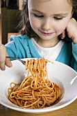 Small girl eating spaghetti with tomato sauce