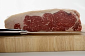 Ein Stück Rinderlende auf Holzbrett mit Messer