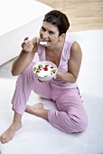 Woman eating yoghurt with kiwi fruit and strawberries