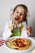 Small girl eating macaroni with tomato sauce
