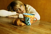 Frau sitzt vor einer Tasse und Laugencroissant