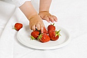 Child's hands reaching for fresh strawberries
