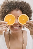 Young woman holding two orange slices in front of her face