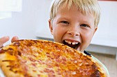 Boy biting into whole pizza