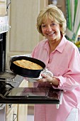 Older woman stood next to oven baking cake