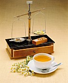 Camomile flowers, a set of precision scales and a cup of camomile tea