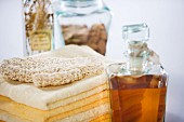 Exfoliating mitt on stack of towels next to bath oil