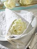 Place-setting with white rose wrapped in napkin